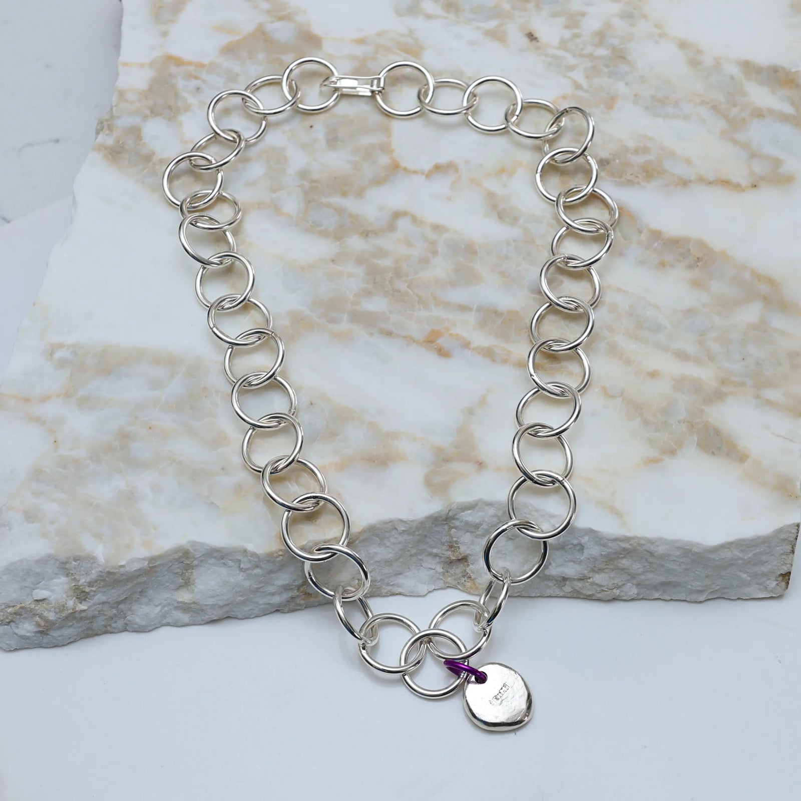 Silver chain bracelet on a white fabric background with driftwood and flowers.