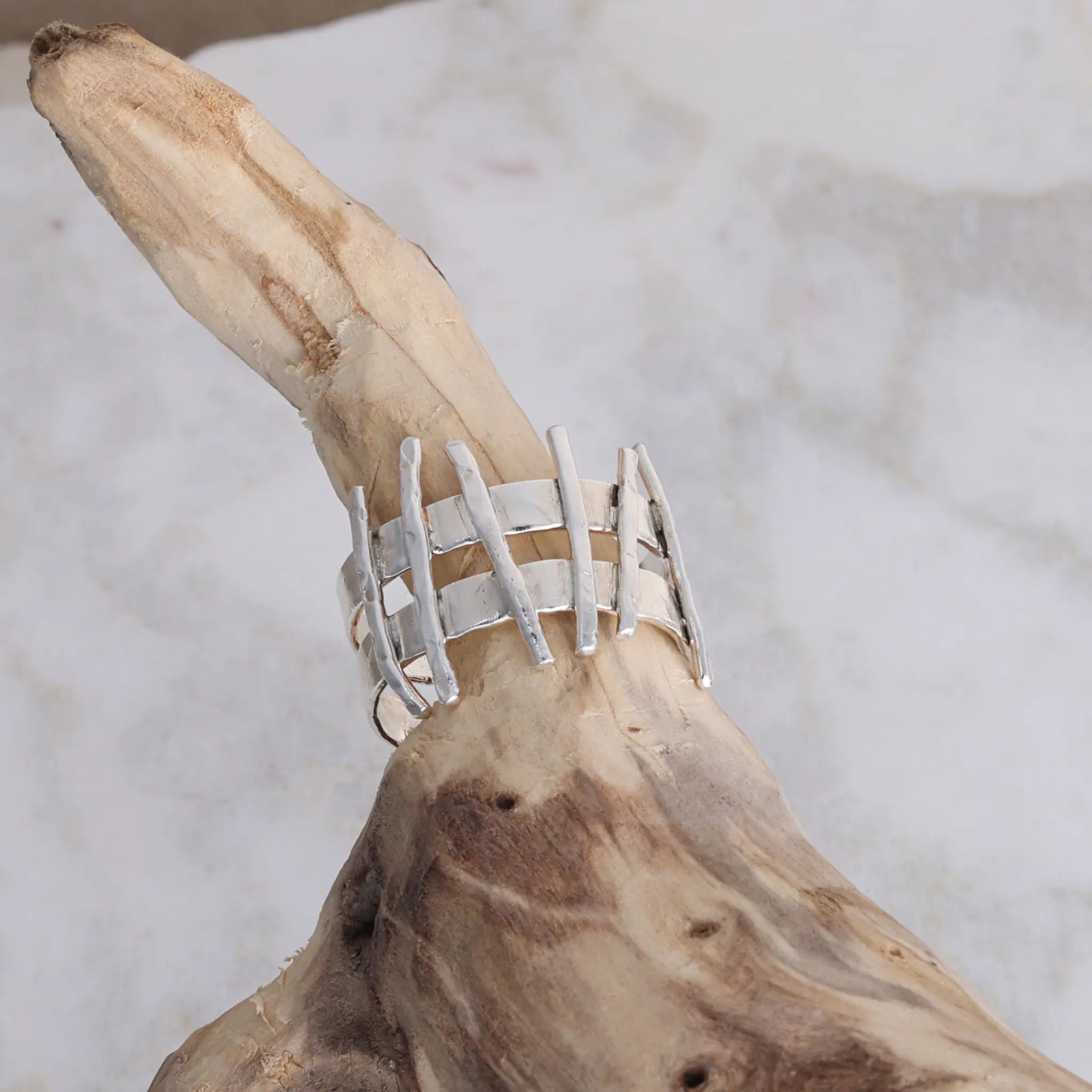 Silver ring with a wavy design on a brown stone against a marble background