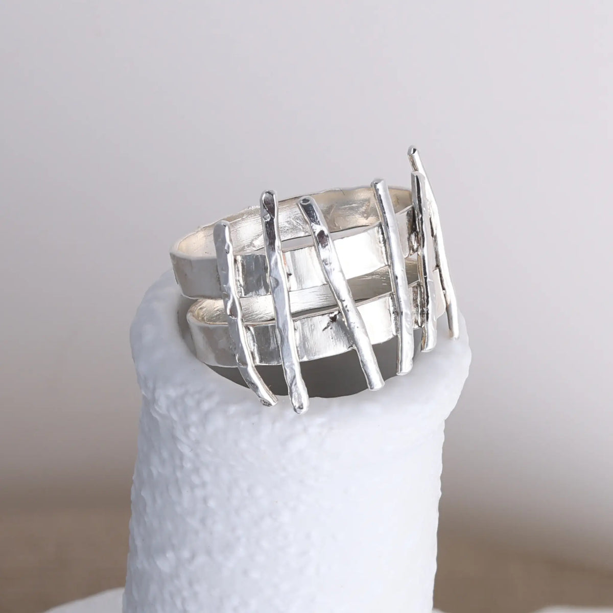 Silver woven ring on a white stand with a plain background