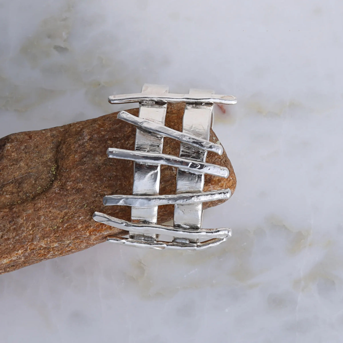 Silver ring with a wavy design on a brown stone against a marble background